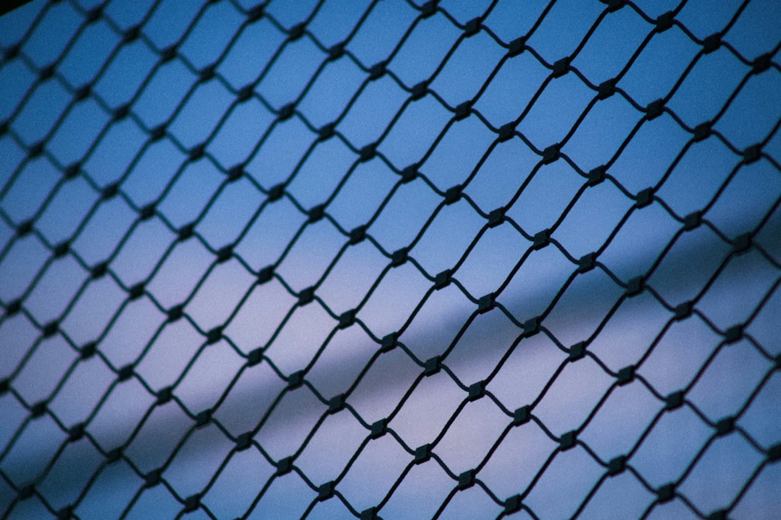 Close view of a chain-link perimeter fence against an evening sky